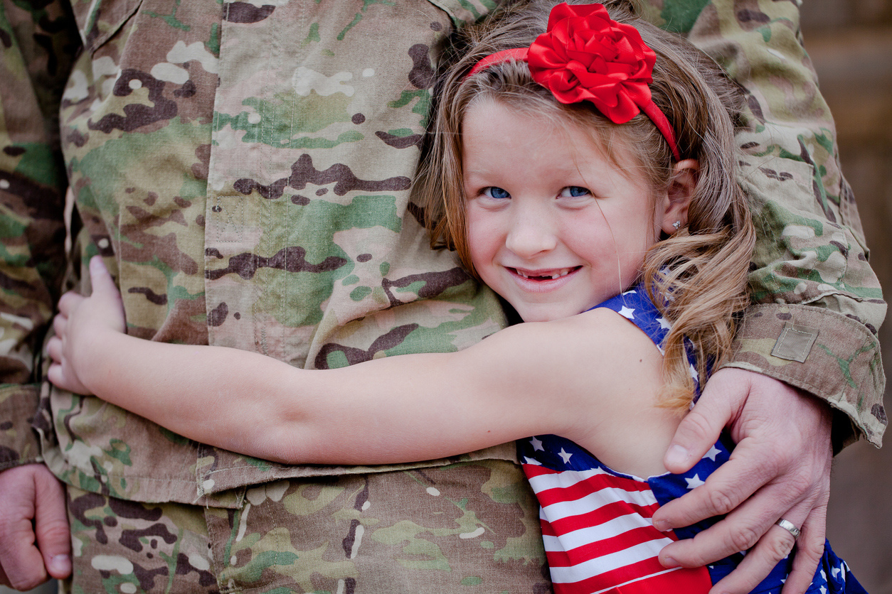 A little girl hugging someone in the military.