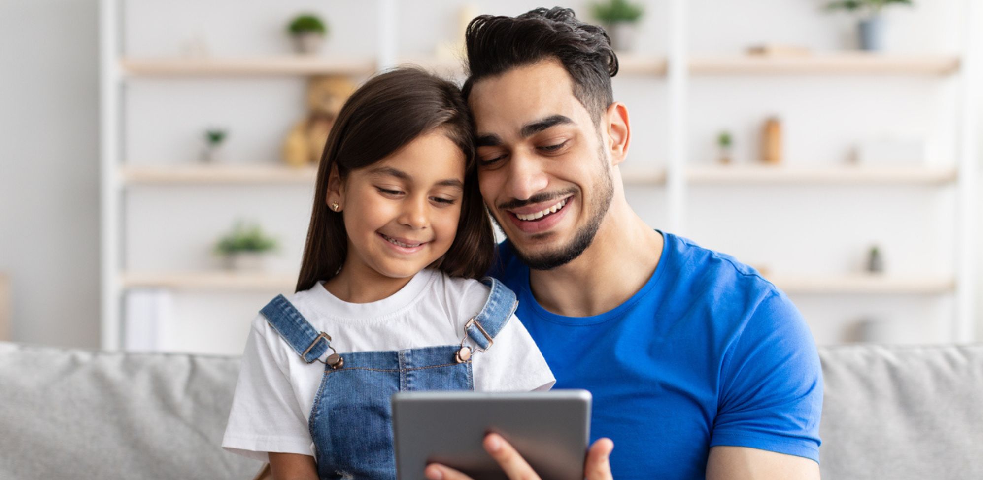 A man and his child smiling and interacting with a tablet.
