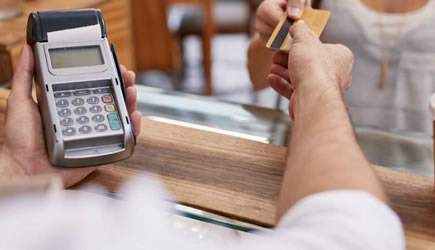 Woman handing merchant a gold credit card to pay for purchase.