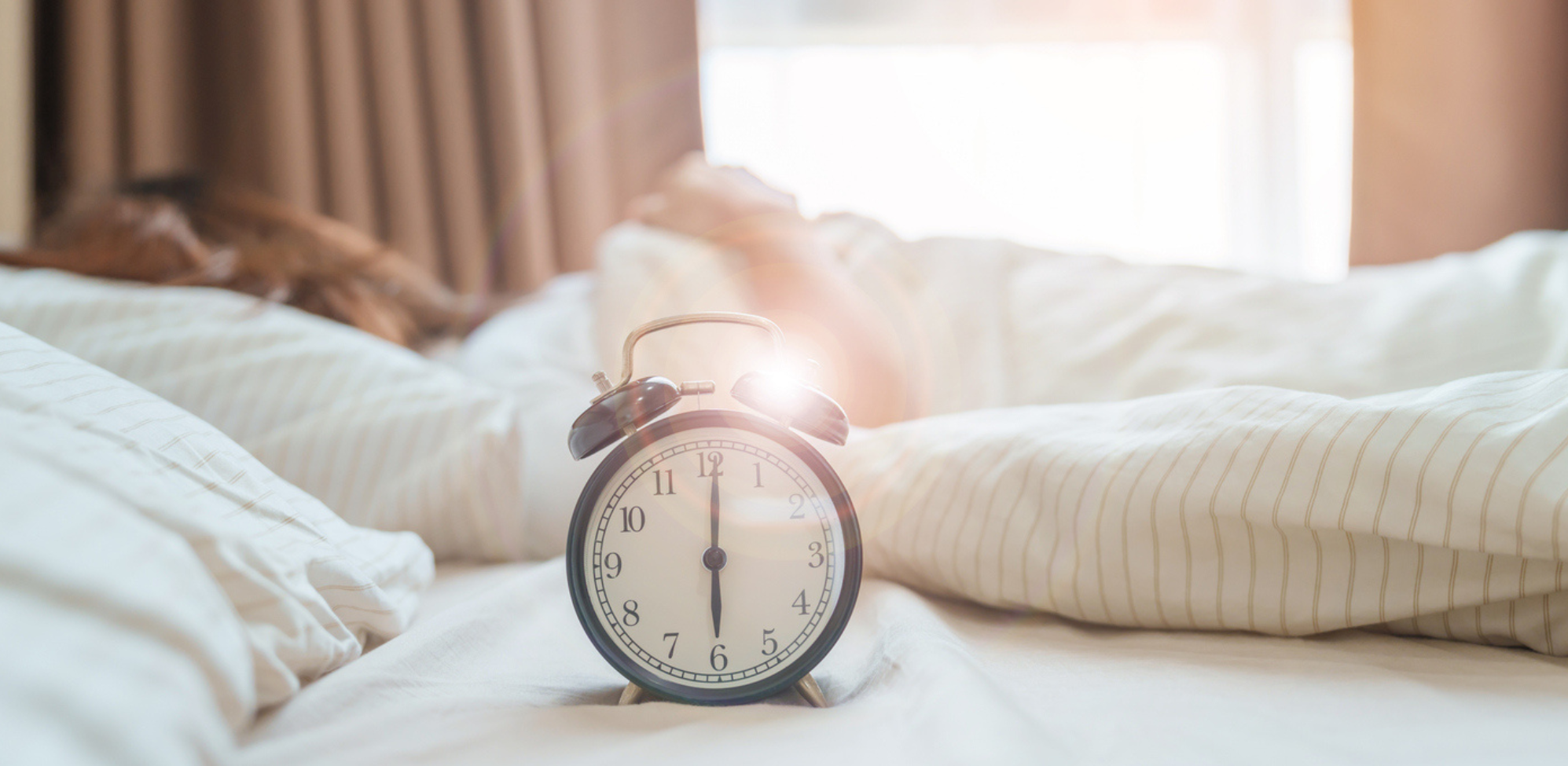 An alarm clock laying on a bed in the morning.
