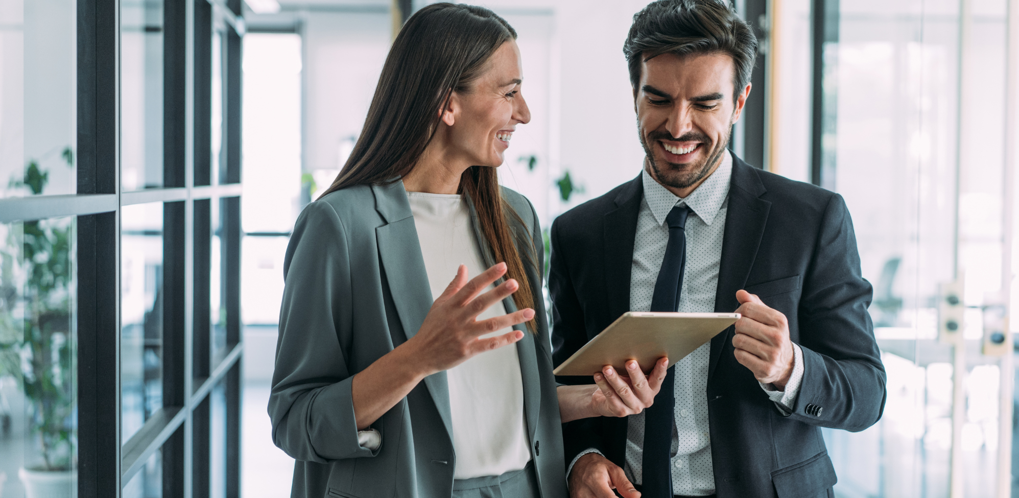 Man and woman in office smiling and looking at tablet
