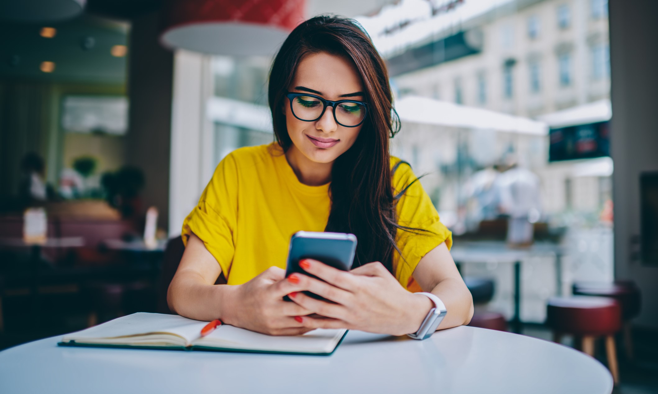 Young girl wearing a yellow shirt is sitting at a local café using Access Bank's mobile banking app.