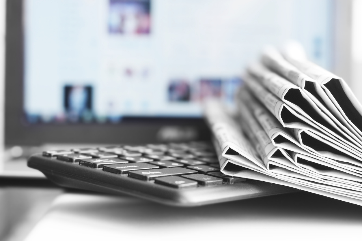 Photo of computer screen with keyboard and pile of newspapers on top.