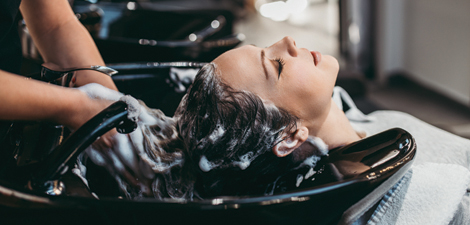 Hair stylist washing a woman's hair at the sink.