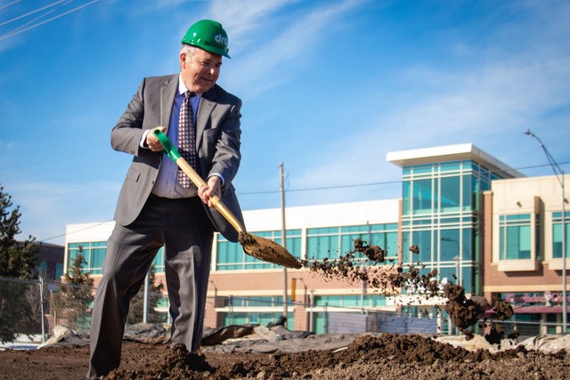 A businessman shoveling dirt outside of a building, taking part in a community event sponsored by ACCESSbank.